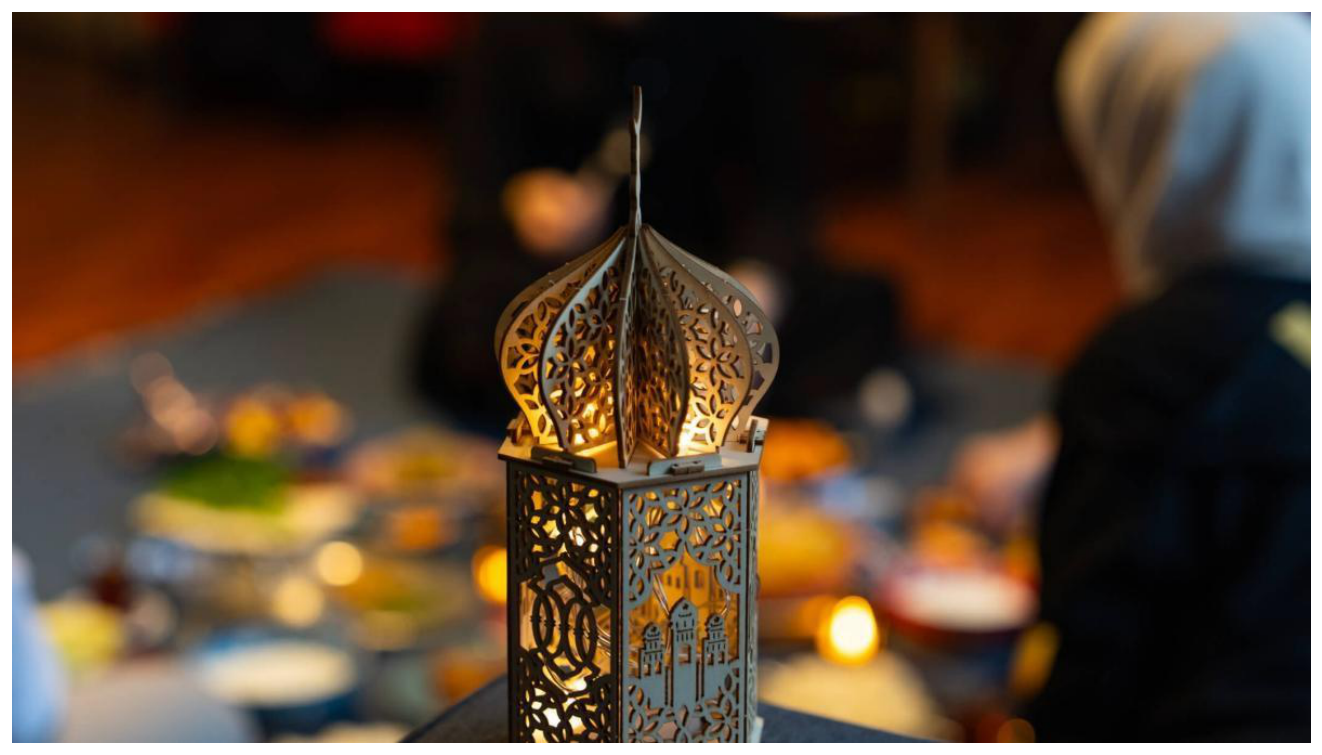 Illustrative image: a lit Ramadan lantern on a table set for a shared meal